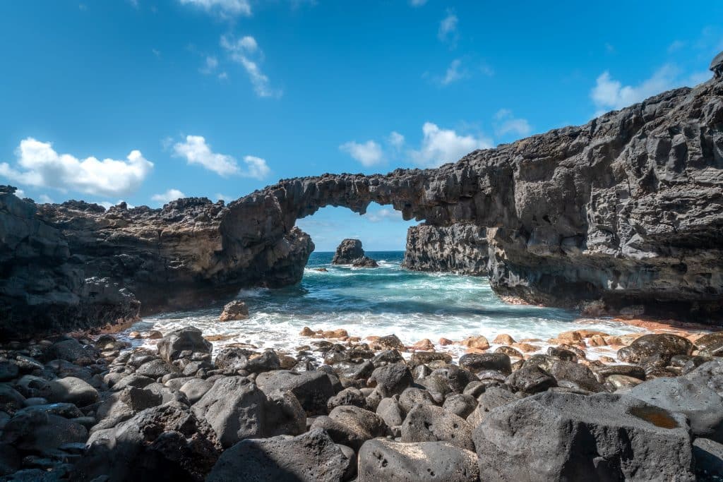 Natürlicher Felsbogen an der Lavaküste bei Las Puntas auf El Hierro mit Brandung und blauem Himmel
