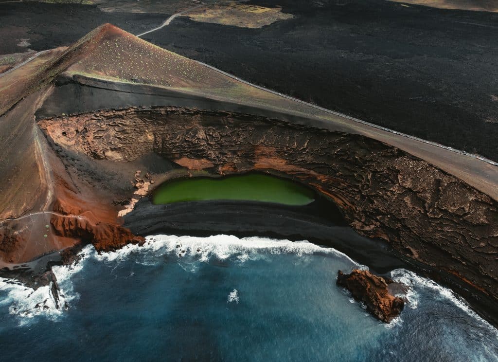 Luftaufnahme des grünen Kratersees El Lago Verde in El Golfo auf Lanzarote mit schwarzem Strand und blauem Atlantik